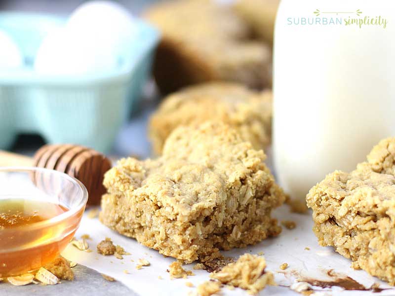 Baked Oatmeal Bars next to a bowl of honey with a glass of milk in the background.