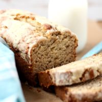 Banana bread with a crumbly topping cut and ready to eat. With a glass of milk in the background.