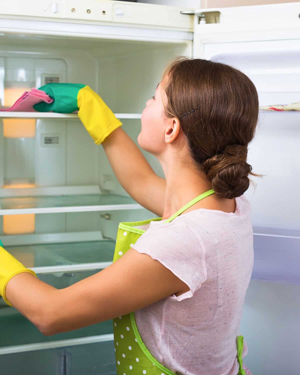 Woman cleaning the inside of a refrigerator with gloves on.