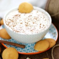 Egg nog dip in a bowl on a plate surround by vanilla wafter cookies and a cinnamon stick.