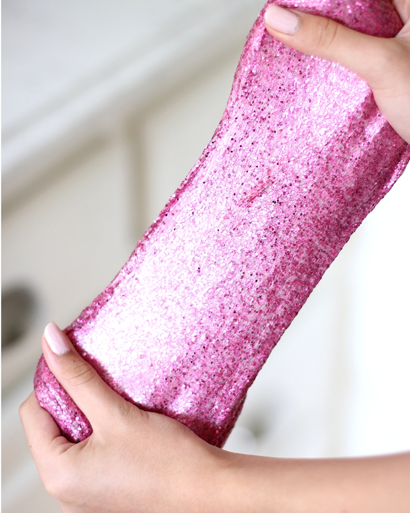 Pink glitter slime stretched by a girl's hands.