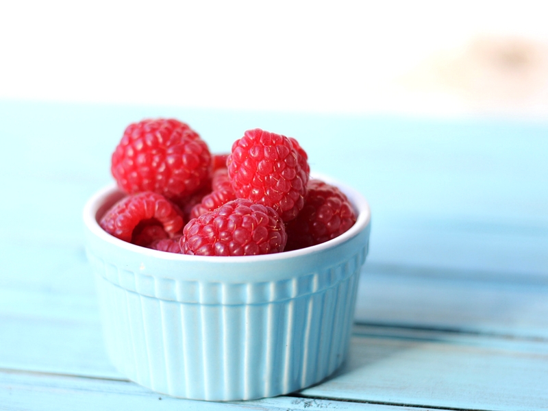 Ripe red raspberries in a small blue bowl.