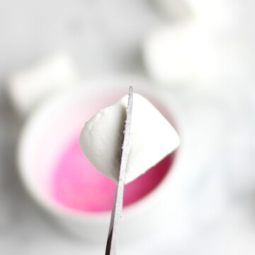 Marshmallow being cut in half for bunny ears with pink sprinkles in the background.