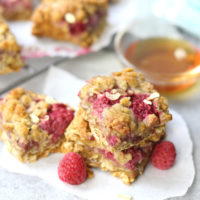 Raspberry oatmeal bars stacked together with fresh raspberry scattered about