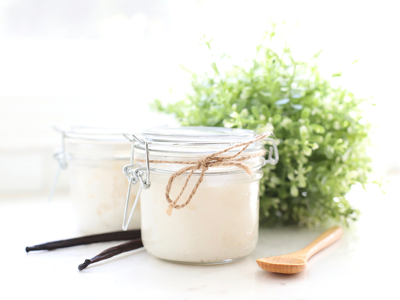 Jar of DIY vanilla sugar scrub with a spoon and vanilla bean next to it.