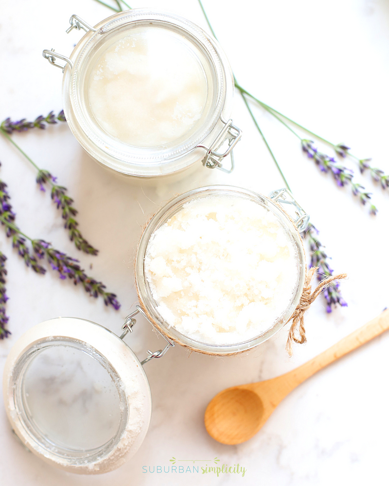 two jars of homemade body scrub with a wooden spoon next to them.
