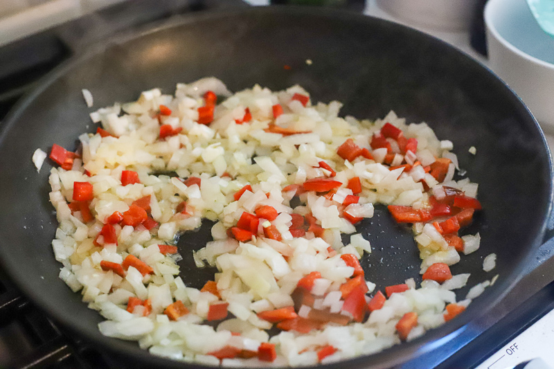 onions and peppers cooking in a pan.