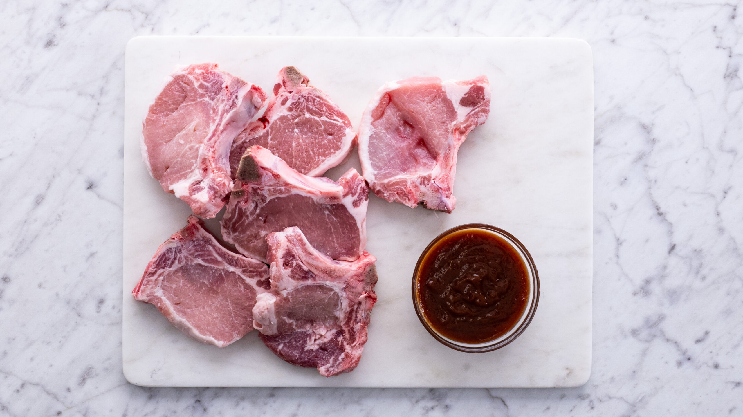 raw pork chops next to bbq sauce