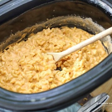 creamy macaroni and cheese in a crockpot with a wooden spoon.
