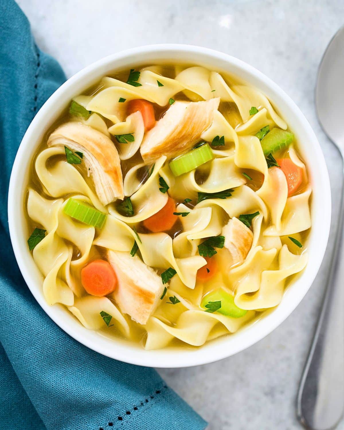 Chicken soup in a bowl with a blue napkin next to it.