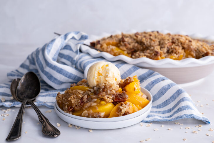 A small plated with peach crisp topped with vanilla ice cream.