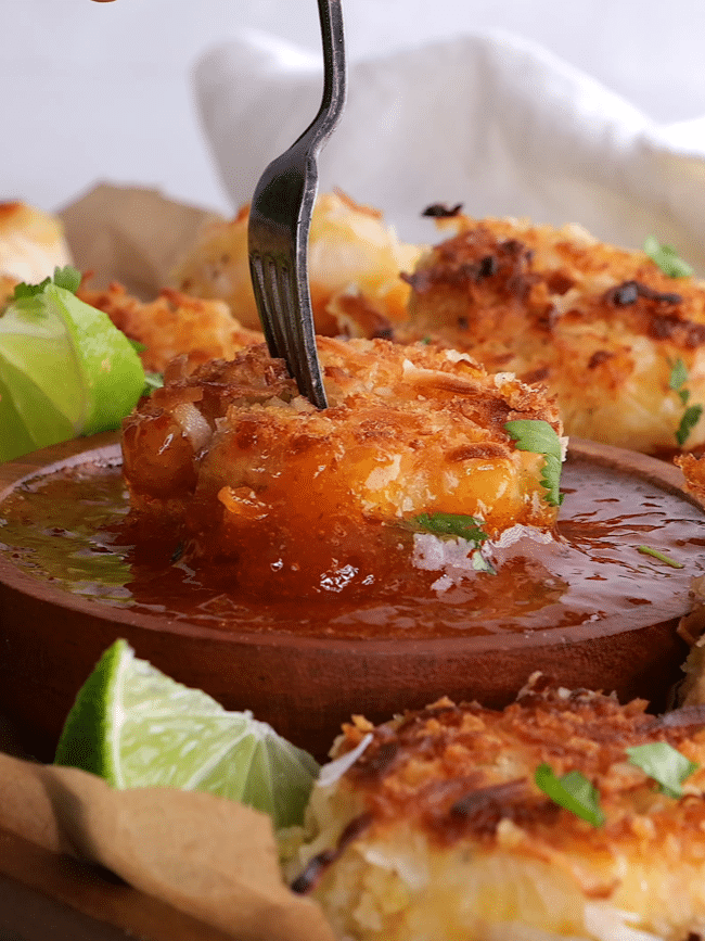 Crispy coconut shrimp being dipped into chili sauce